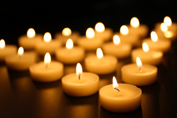 Obraz na płótnie Canvas Alight candles in a row on black background, blurred