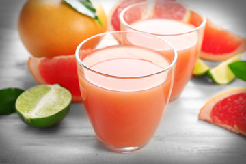 Two glasses of citrus juice and fresh fruits on light wooden background