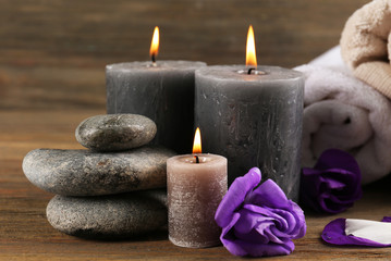 Obraz na płótnie Canvas Alight wax grey candles with flowers, towels and pebbles on wooden background - relax set
