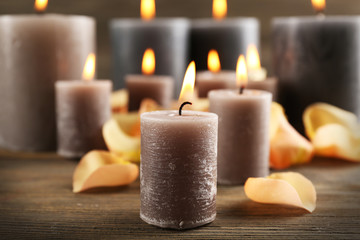 Alight wax grey candle with flower petals on wooden background