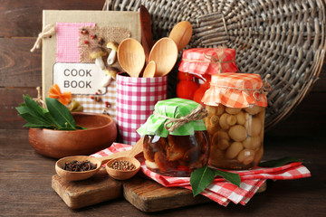 Jars with pickled vegetables, beans, spices and kitchenware on wooden background