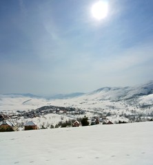 Beautiful, idyllic snowy winter landscape in the mountains, on a crisp sunny morning, with snow-covered rooftops of a small picturesque village. Vertical panorama.