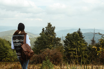 beautiful happy stylish traveling girl in the mountains on a background of a forest