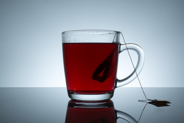 tea bag in a transparent mug with reflection on a grey background