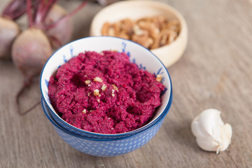 Obraz na płótnie Canvas Beetroot pesto in a white bowl on a wooden table with garlic beetroot and rice cakes on the back, selective focus