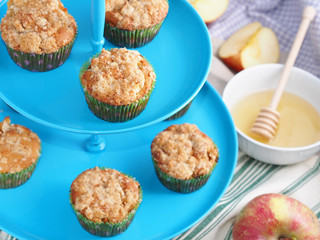 Apple crumb spiced muffins on blue muffin stand with table napkins, apples and a bowl with honey in the background