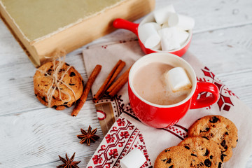 
winter mood , cocoa with marshmallows in a red cup , cinnamon and cookies with chocolate on a wooden background