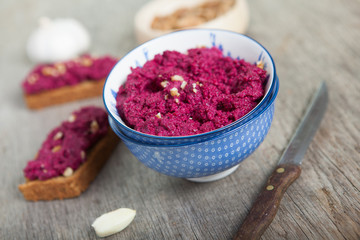 Obraz na płótnie Canvas Beetroot pesto in a blue bowl on a wooden table with garlic beetroot and almond bread on the back, selective focus