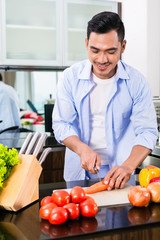 Asian man cutting salad in kitchen