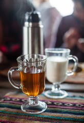 Two glasses cups with tea and milk and thermos on table