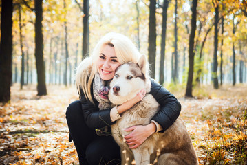 young beautiful female having fun with siberian husky in autumn park