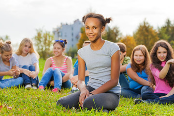 African girl and friends sitting on green meadow