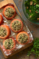 Vegetarian baked tomato stuffed with quinoa, mushroom and parsley with spinach and walnut salad on the side, photographed overhead  on slate with natural light