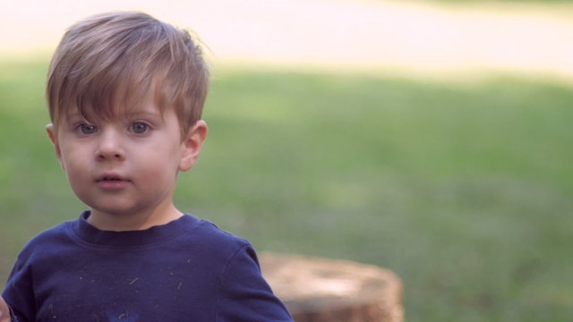 Little blond 3 year old boy looking at camera waving, smiling, and playing with toy in slow motion outside in green yard.