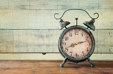 image of vintage alarm clock on wooden table in front of wooden background. retro filtered
