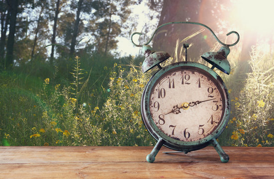 image of vintage alarm clock on wooden table in front of rustic country side landscape background. retro filtered
