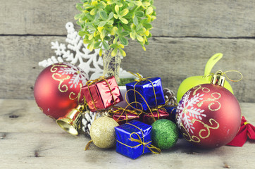 cropped image of red ball, artificial tree on pot, pine cone, white snowflakes, golden bell, red and blue gift box on wooden floor