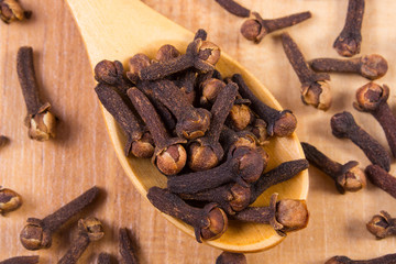 Heap of cloves with wooden spoon on table, seasoning for cooking