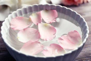 Tender pink rose petals in a bowl of water on wooden background