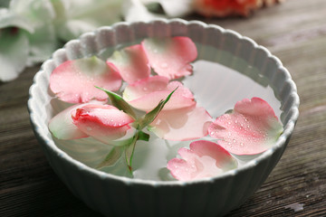 Obraz na płótnie Canvas Tender pink rose and petals in a bowl of water on wooden background