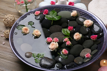 Spa composition of candles, flowers and stones in water, on wooden background