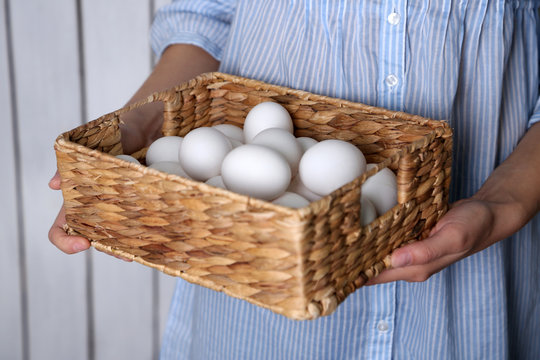 Eggs in basket in women hands on wooden background