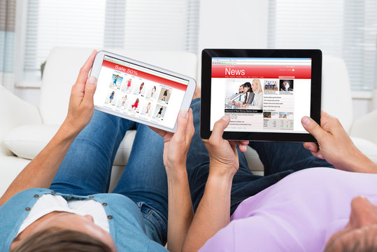 Couple Online Shopping And Reading News On Digital Tablets