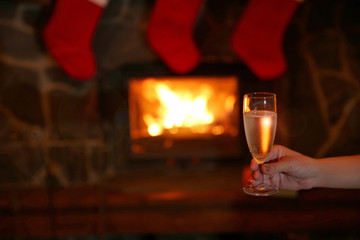 Female hand with glass of sparkle wine on fireplace background