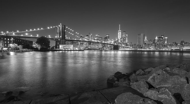 Black and white photo of Brooklyn Bridge and Manhattan waterfront at night, NYC, USA