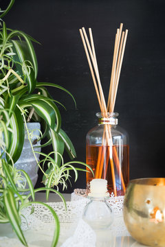 Aroma reed diffuser, candle, lace and spider plant against blackboard wall. Selective focus on thebottle and sticks.