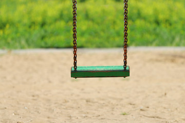 Green woioden swing on chain on playground at summer day