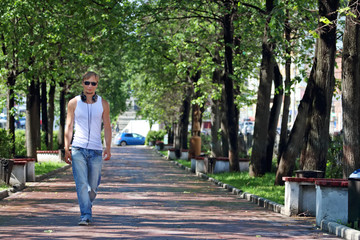 Fototapeta na wymiar Man in sunglasses goes on alley with green trees and benches 