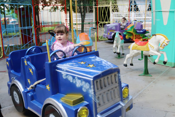 Obraz na płótnie Canvas Little beautiful girl rides in car of carousel in amusement park
