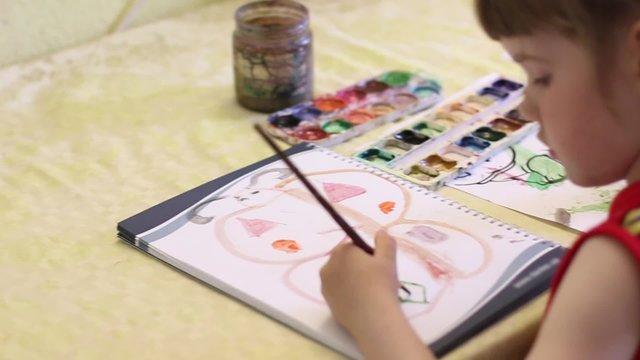 Little girl painting butterfly in notebook at table. Close up
