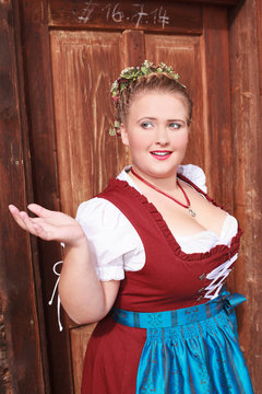 Portrait einer unschlüssigen jungen bayerischen Frau im Dirndl mit großen Dekollete , geflochtenem Haar und Blumenkranz auf dem Kopf, Oberkörperansicht.
