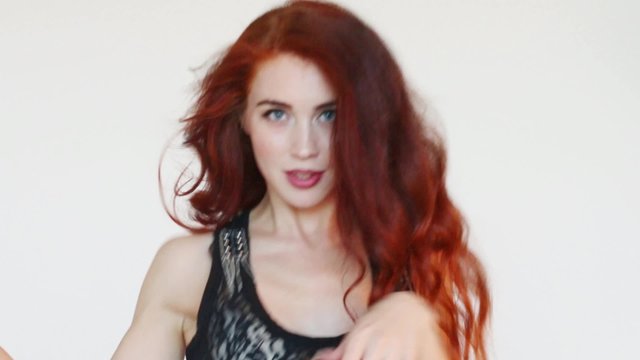 Beautiful woman with red hair dances in white studio
