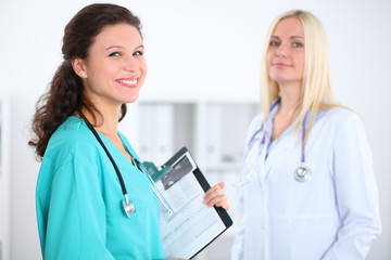 Beautiful young smiling female doctor standing at hospital with doctor on the background. Medical...