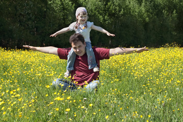 Happy young man with little daughter among yellow flowers 