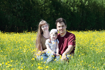 Fototapeta premium Mother, father and daughter among yellow flowers at meadow