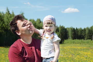 Young father holds happy little daughter near green forest 