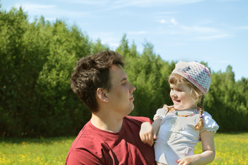 Young father looks at happy little daughter near green forest 