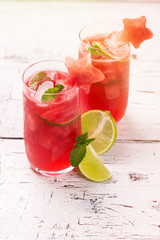 Watermelon and lime fresh in high glasses decorated by watermelon stars on white wooden table. Selective focus