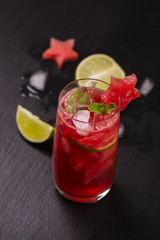 Watermelon and lime fresh in high glasses decorated by watermelon stars on black stone table. Selective focus