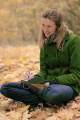 Girl in autumn leaves with a notebook