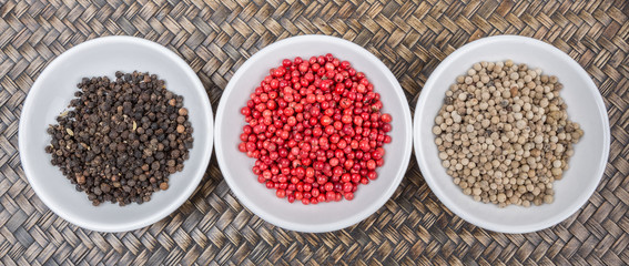Black, white and pink peppercorn in white bowl over wicker background