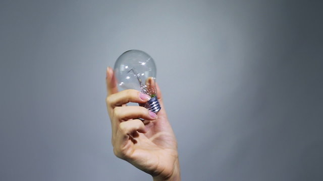 Female hand holds and turns the light bulb. White Background.