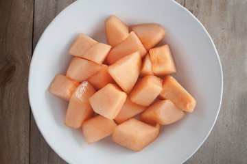 closeup melon slice in white dish with wood table background