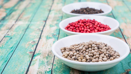 Black, white and pink peppercorn in white bowl over wooden background