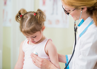 Pediatrician woman examining cute little girl with stethoscope. Kid looks sad and sick
