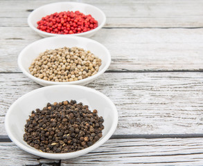Black, white and pink peppercorn in white bowl over wooden background